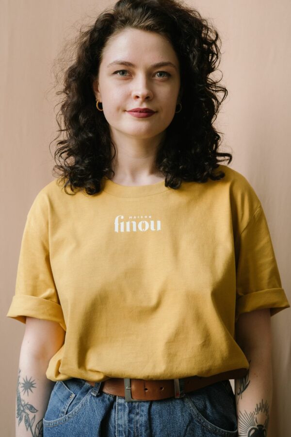 Femme portant un t shirt jaune moutarde unisexe manches courtes floqué Maison Finou à la coupe droite et col rond