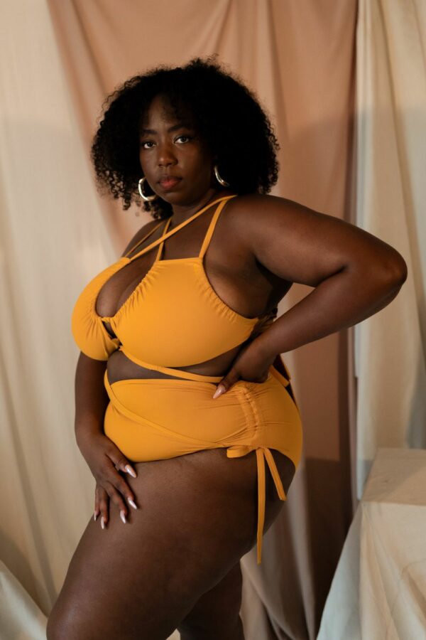 Femme debout portant un maillot de bain une pièce jaune moutarde de la marque Maison Finou. Il est à nouer de multiples manières