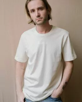 Homme portant un t-shirt écru manches courtes floqué Maison Finou à la coupe unisexe, droite et col rond
