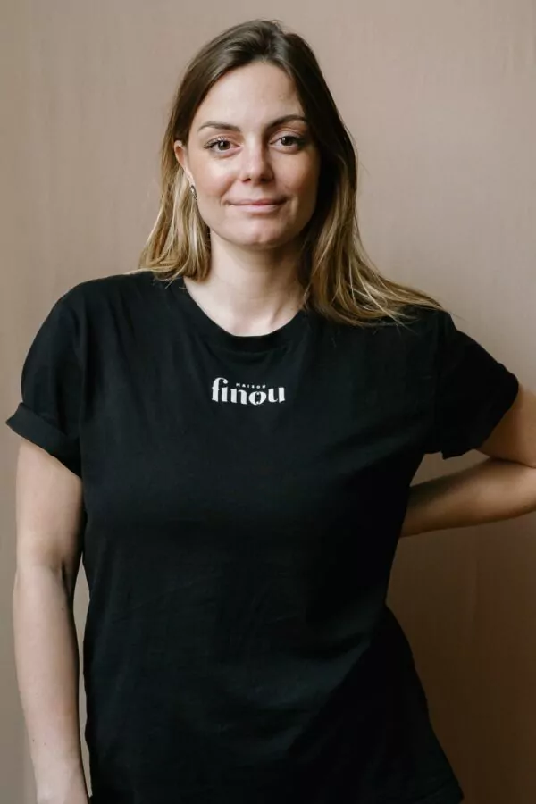 Femme portant un t-shirt noir, manches courtes, floqué Maison Finou unisexe, au col rond et à la coupe droite
