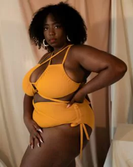 Femme debout portant un maillot de bain une pièce jaune moutarde de la marque Maison Finou. Il est à nouer de multiples manières